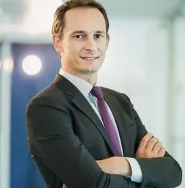 Person in a suit with arms crossed, standing confidently indoors.