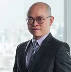 Bald man in a suit and tie with glasses smiling indoors.