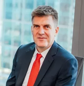 Man in a suit and red tie sitting by a window.