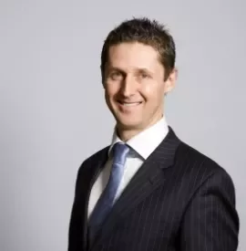 Man in a suit smiling against a gray background.