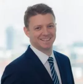 Smiling man in a suit with a cityscape background.