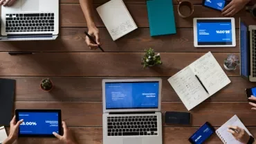 People working with laptops and tablets on a wooden table.