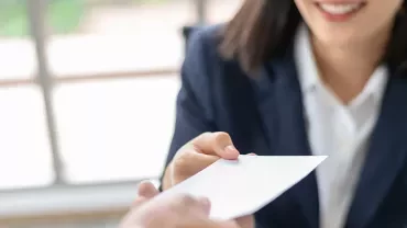 Woman handing over a business card in an office setting.