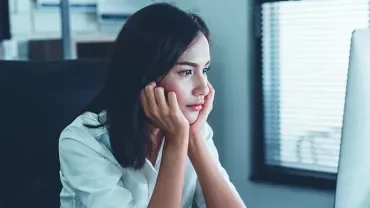 Woman in white shirt looking intently at a computer screen in an office.