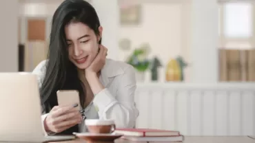 Woman smiling at her phone near a laptop with coffee