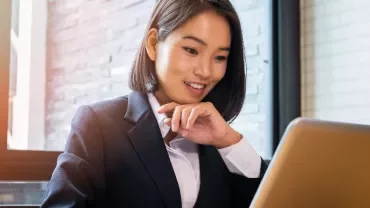 Businesswoman in a suit working on a laptop by a window.