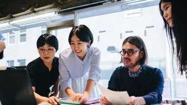 Group of people collaborating around a laptop in an office setting.
