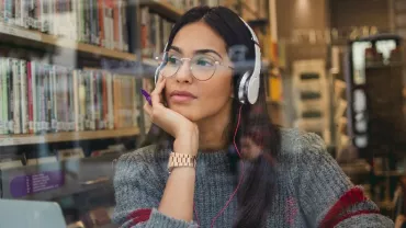 an East Asian woman in glasses looking out of a cafe, with headphones on