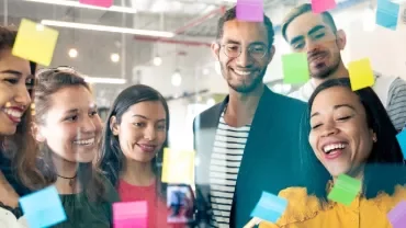 A group of diverse coworkers brainstorming with sticky notes on a glass wall.