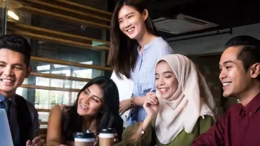 Group of people smiling and looking at a laptop in a modern office.