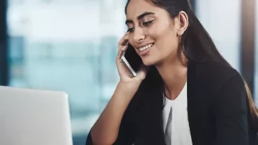 Smiling woman talking on phone while working on a laptop.