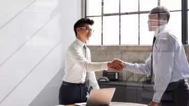 Two business professionals shaking hands in a bright office.