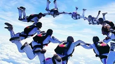 A group of skydivers forming a circle in mid-air against a cloudy sky.