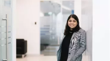 Woman standing in an office hallway, wearing a patterned jacket.