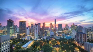 A vibrant city skyline at dusk with colorful skies and illuminated skyscrapers.