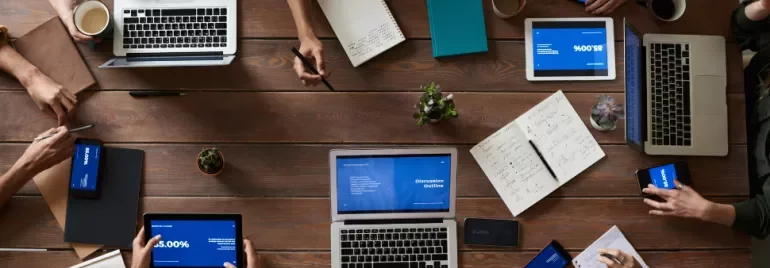 People working with laptops and tablets on a wooden table.