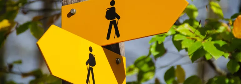 Yellow hiking trail signs with silhouettes of hikers in a forest.