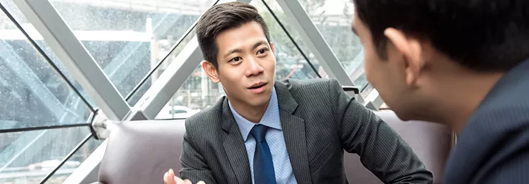 Two men in business attire having a conversation in a modern office setting.