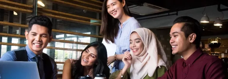 Group of people smiling and looking at a laptop in a modern office.
