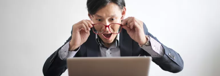 An Asian, white-collar professional holding out his glasses for a better look at his laptop screen