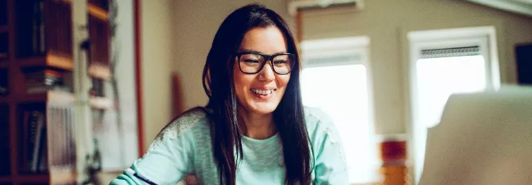 East Asian female professional smiling as she works on the laptop.