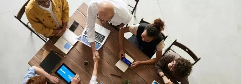 A group of professionals engaged in leadership networking, sitting around a table with laptops and tablets