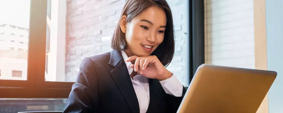 Businesswoman in a suit working on a laptop by a window.