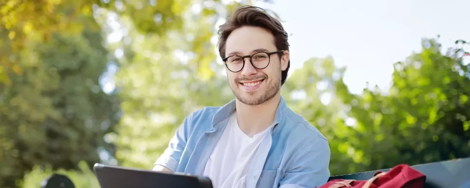 Smiling person with glasses sitting outside on a sunny day