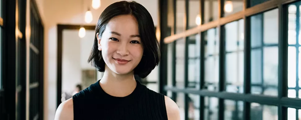 Person smiling in a modern office hallway with glass doors.