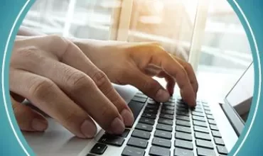 Hands typing on a laptop keyboard in a brightly lit room.