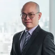 Bald man in a suit and tie with glasses smiling indoors.