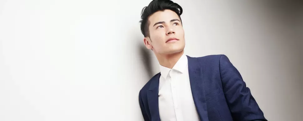 Man in blue suit and white shirt, looking upwards against a white background.