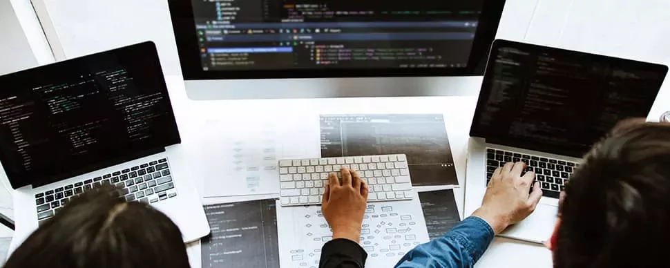 Developers coding on laptops and desktop with technical diagrams.