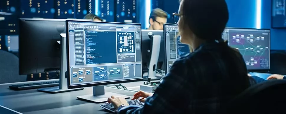 Person working at a computer station with code on screens.