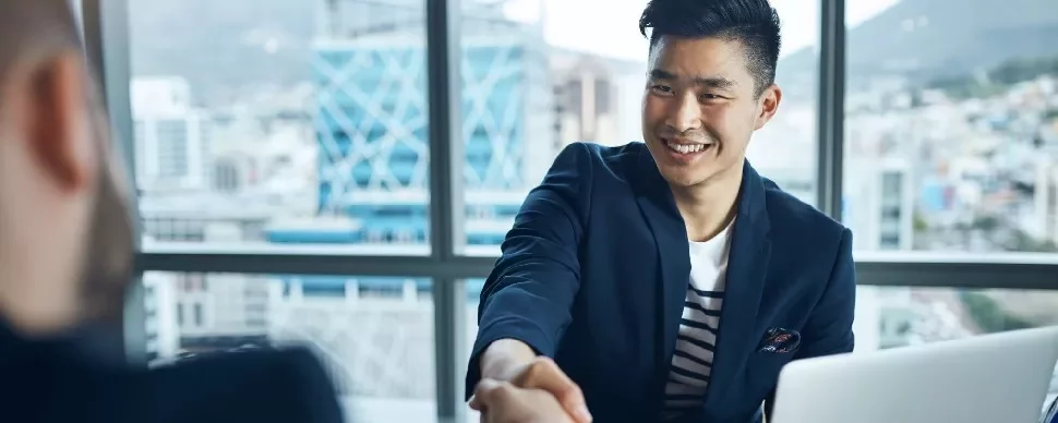 Smiling man in a suit shakes hands in an office setting.