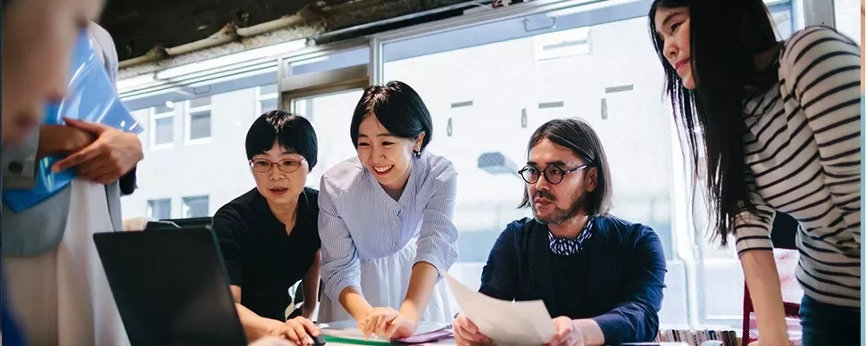 Group of people collaborating around a laptop in an office setting.