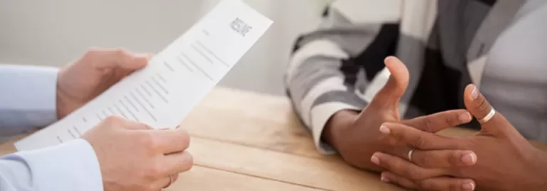 Two people at a table during a job interview, one holding a resume.