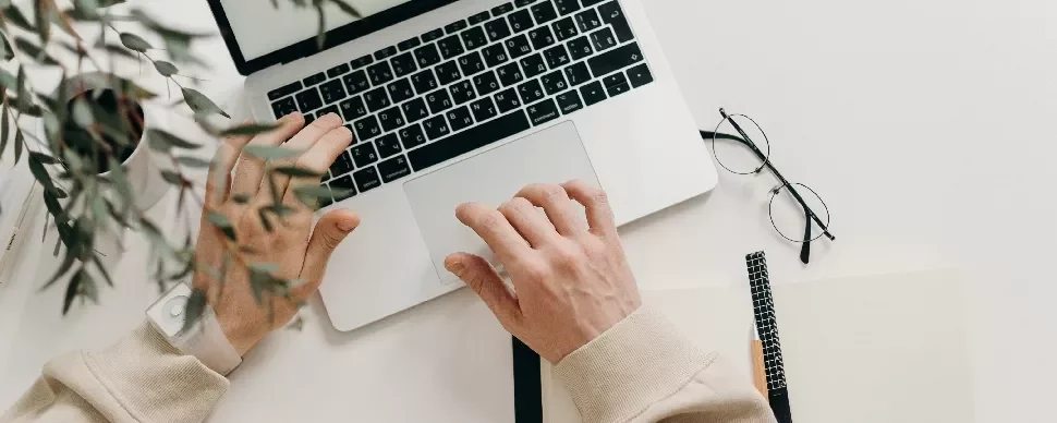 Person working on a laptop with glasses and a notebook on the table.