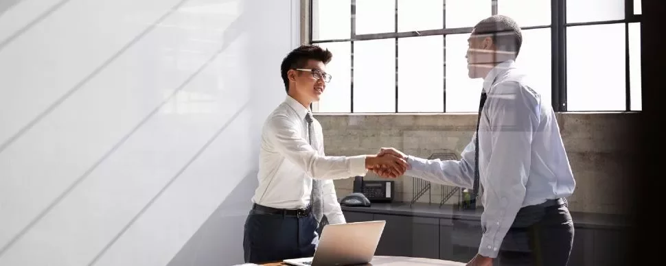 Two business professionals shaking hands in a bright office.