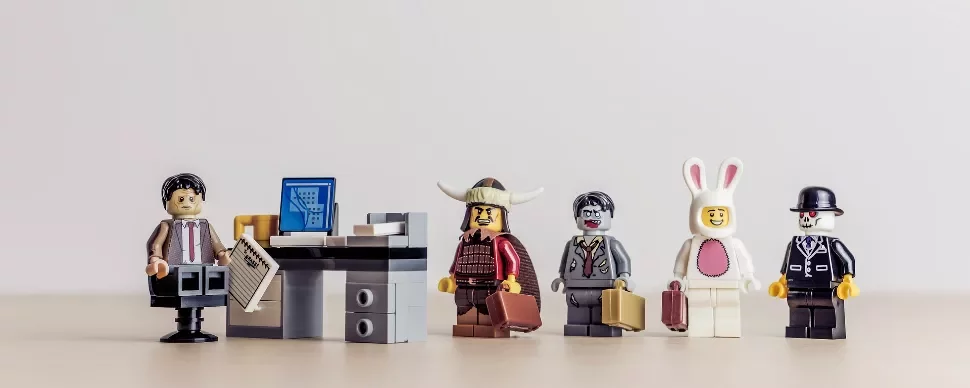 LEGO minifigures lined up, one in an office, others in costumes with briefcases.