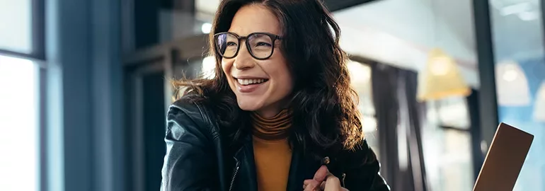 Smiling woman in glasses sits at a table indoors.