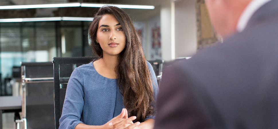 An Asian female worker sitting across a person wearing a grey suit in an office setting.